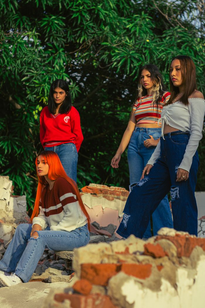 Four fashionable women posing in a natural, semi-urban setting with broken bricks.