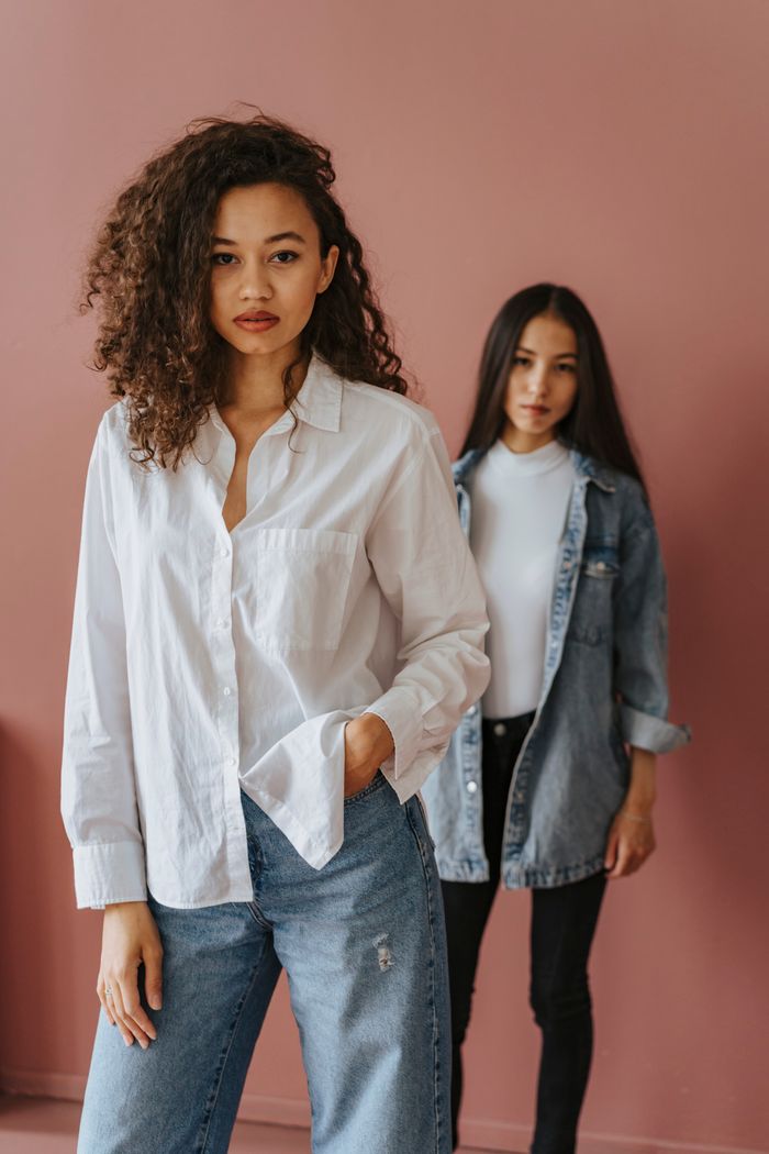 Chic portrait of two young women in casual fashion against a pink background.