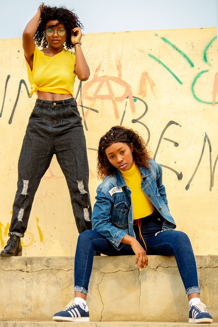 Young trendy African American girlfriends in trendy clothes looking at camera near graffiti wall on street